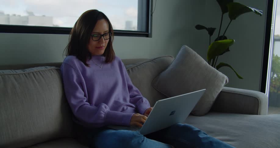 Woman sitting couch typing on laptop in living room