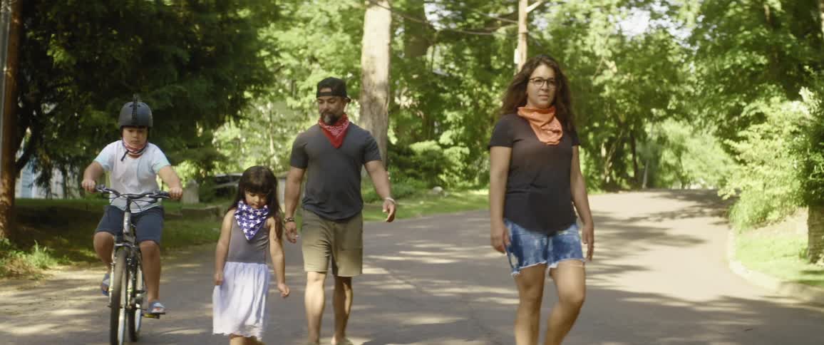 A man a woman a girl and a boy on a bicycle on a path in a park with trees and the sky in the background