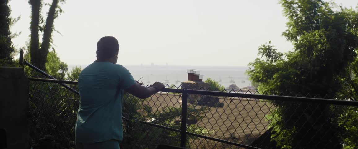 A man standing by a fence with trees the sky and clouds in the background