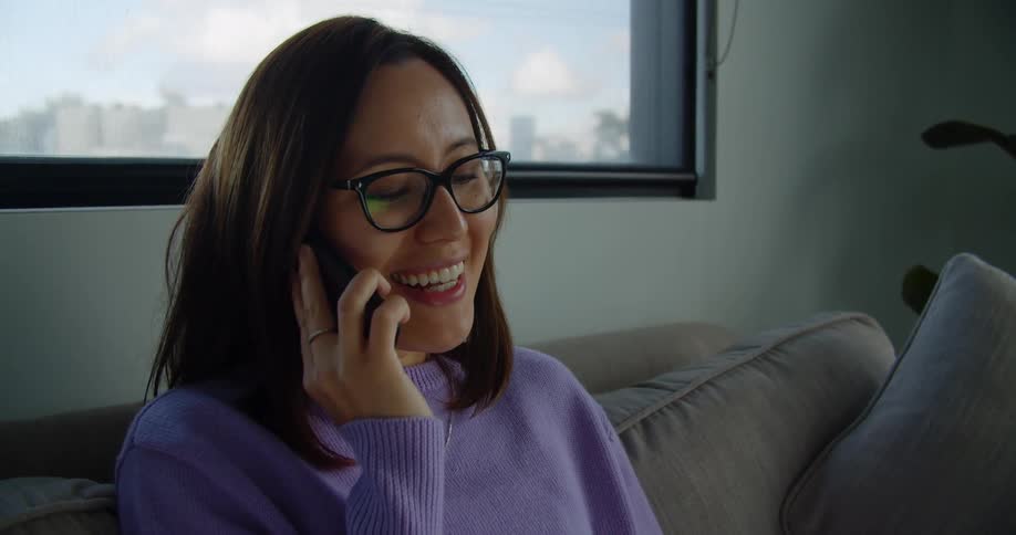A woman sitting at home on her couch talks on her cell phone