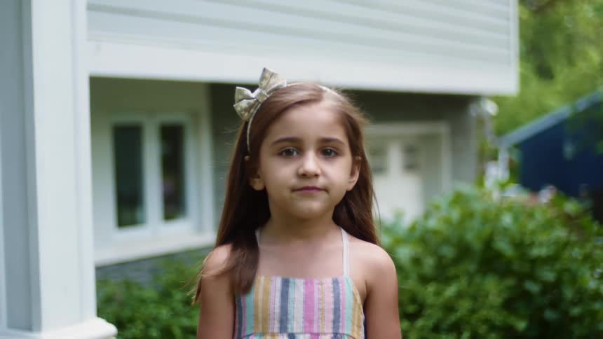 Happy little girl standing in front of a house smiling