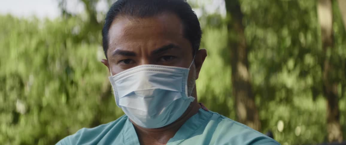 Man wearing a facial mask posing outdoors near trees