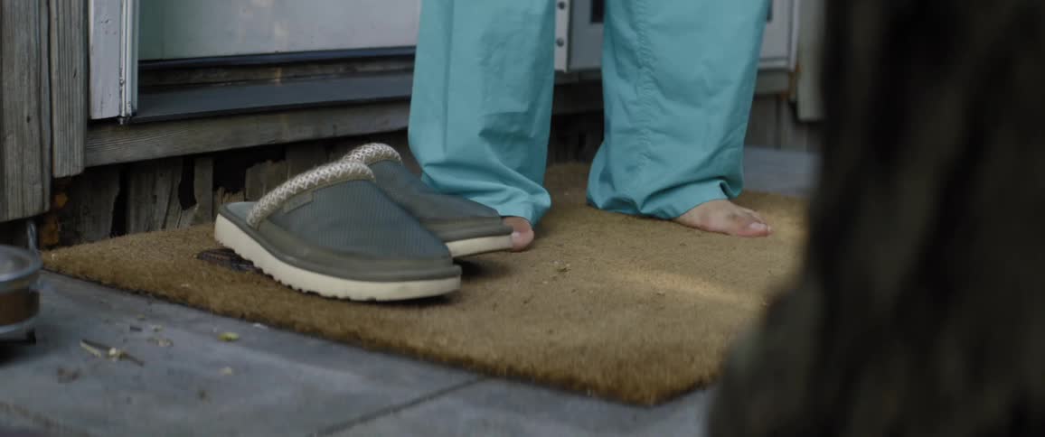 A person wearing surgical scrub pants steps out of a residential home and slips their feet into some slippers