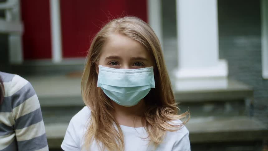 A girl with a mask sitting on a porch with a house and door in the background