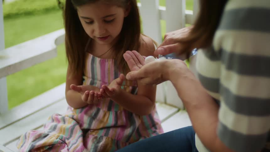 A mother puts hand sanitizer in her daughters hand and her own while sitting on a porch swing