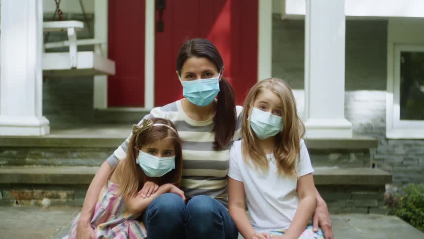 Mother and daughters wearing facial masks sitting on front porch