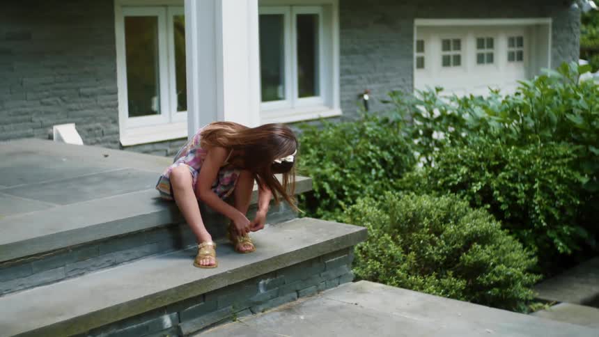 Girl in a dress ties her sandals sitting in the porch of a house