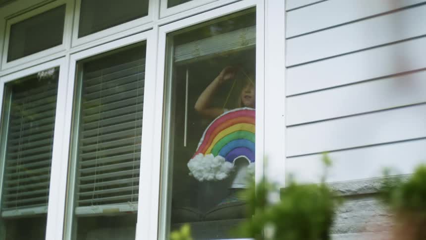 A girl hanging up a decoration of a rainbow by a window