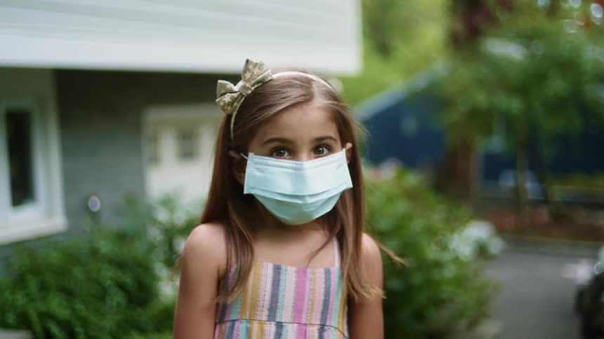 Little girl wearing a facial mask posing in front of a house