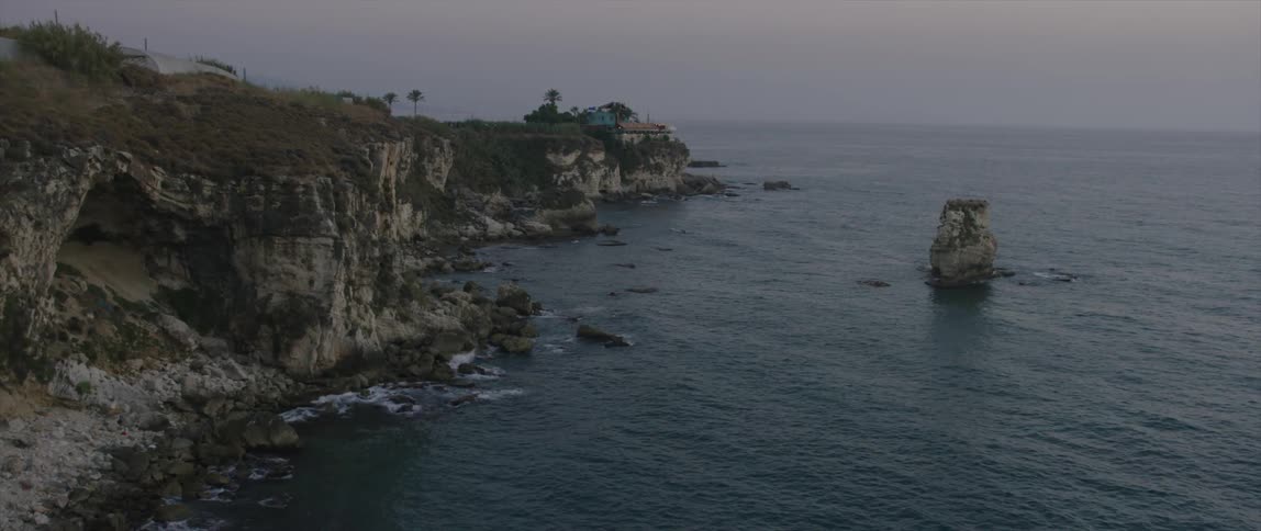 View of a home on a cliff as waves crash against the rocks below