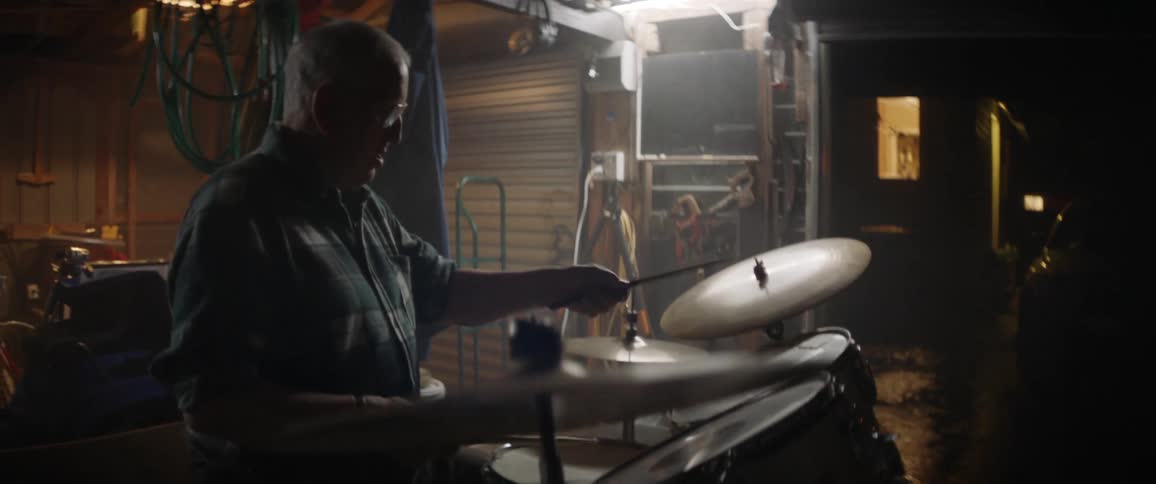 An older man is playing drums in his garage
