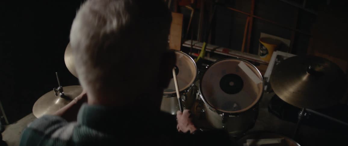 Man drums on a drum set in a dimly lit room