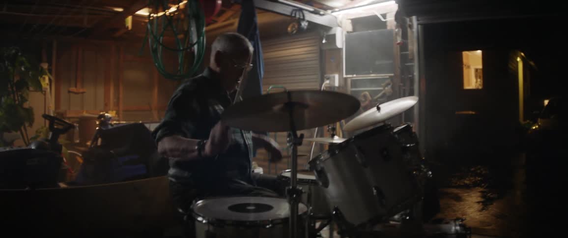 An older man is playing drums in his garage