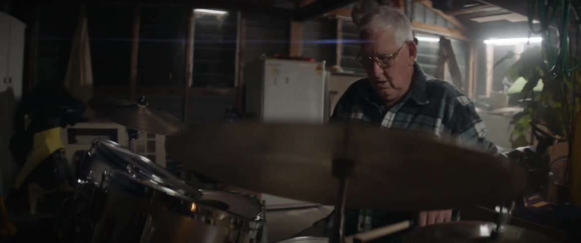 An older man is playing drums in his garage