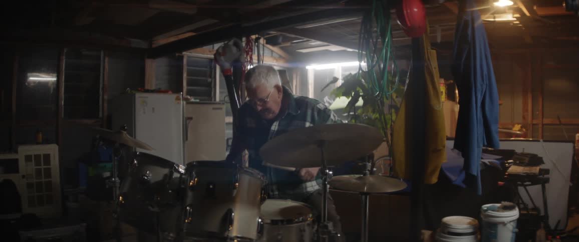 An older man is playing drums in his garage
