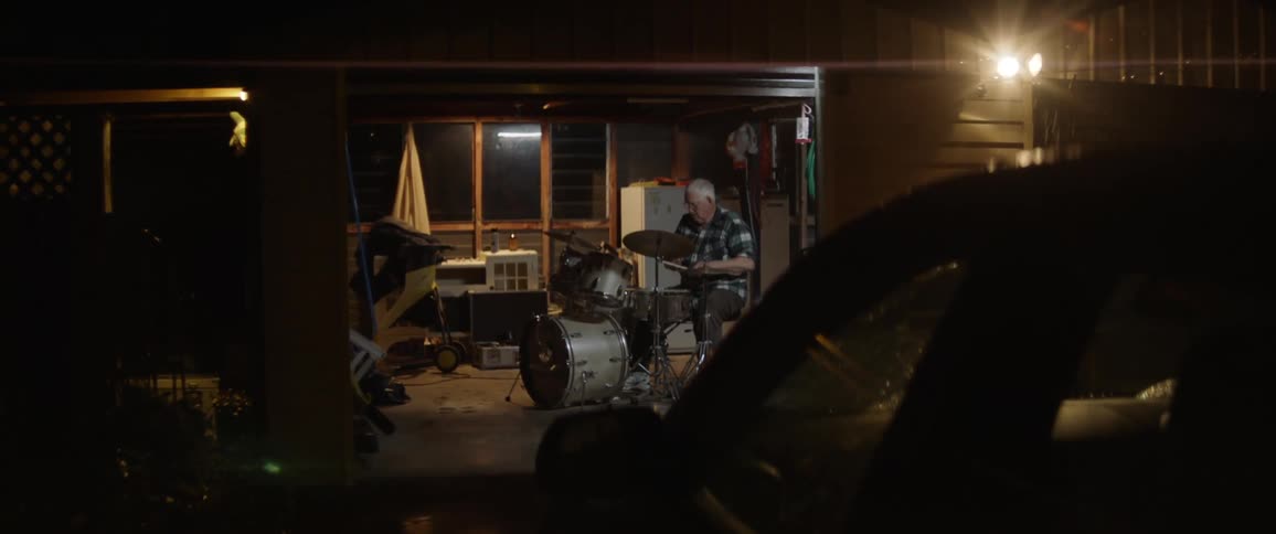 A man is playing the drums by his garage at night