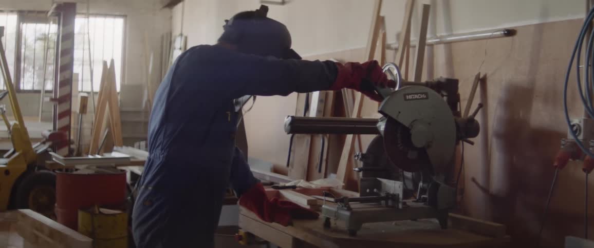 A man is using a circular saw as he works at a workbench inside during the day