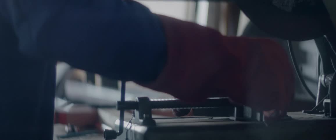 A worker wearing gloves clamps a piece of metal into place