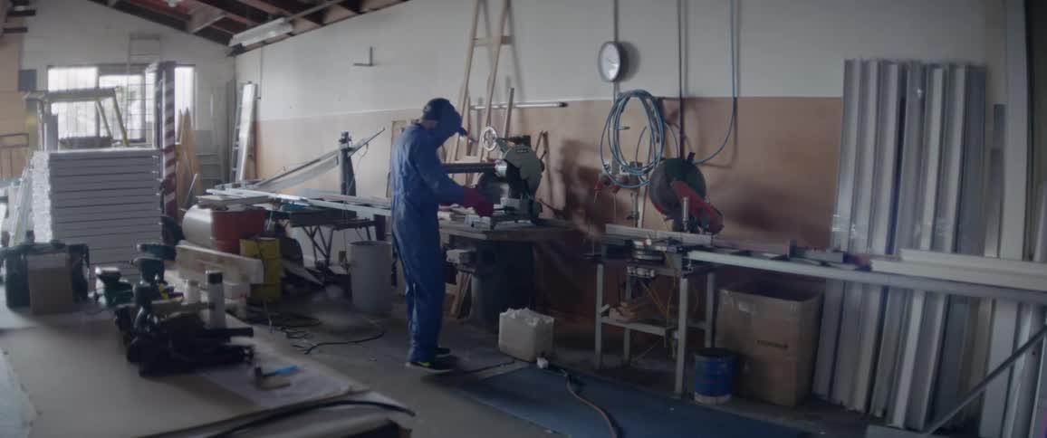 A man is flipping down his protective mask as he approaches a workbench during the day