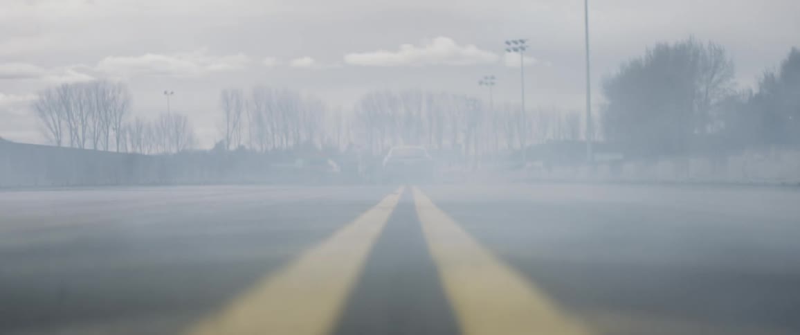 Smoke pours out of a car's exhaust as it drives down the road