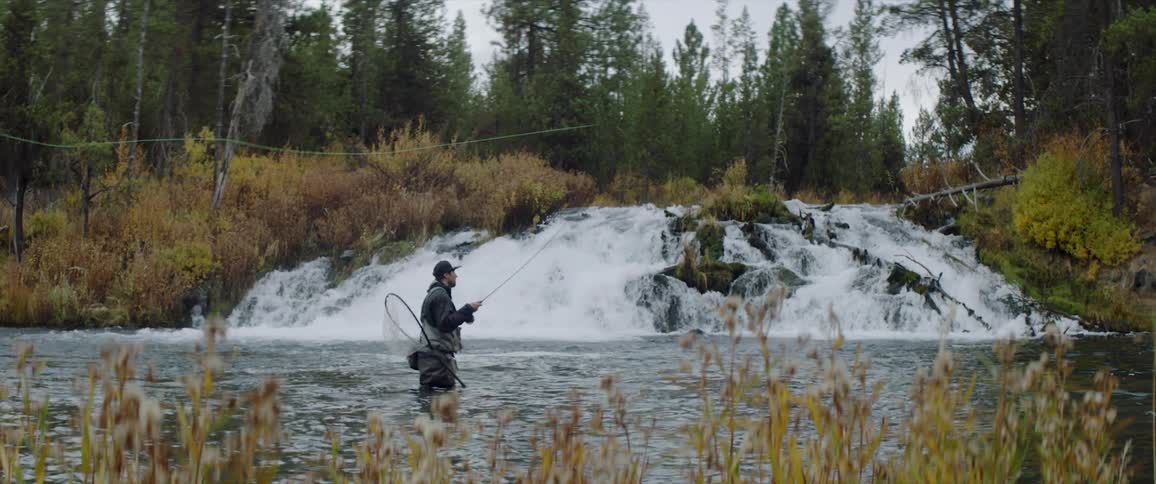 A man is standing in a small river fly fishing