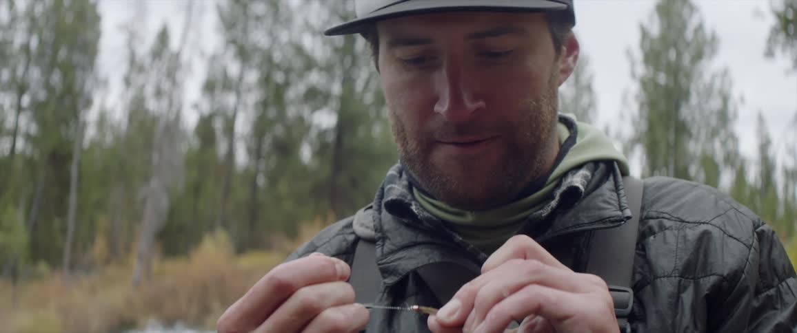 A man is wrapping a lure as he fishes in a river during the day
