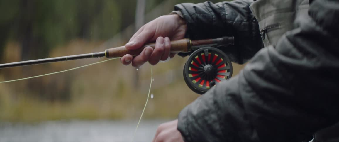 A man lifts the string and pulls the wheel on the fishing pole