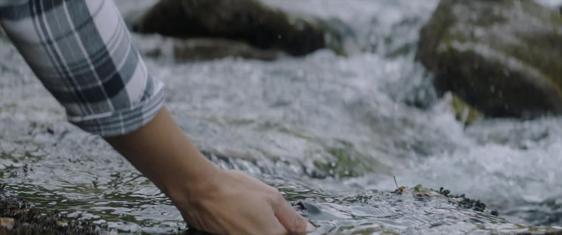 A hand is reaching into a stream to scoop up some water