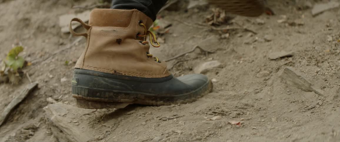 Person hiking up a dirt hill wearing brown boots