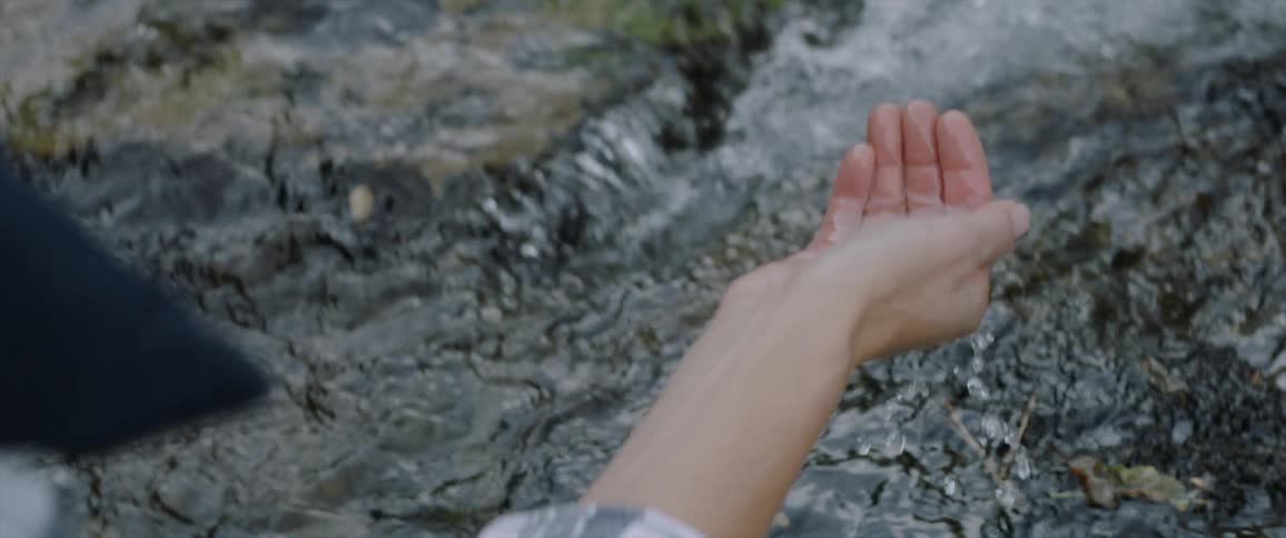 Woman scoops stream water with her hand
