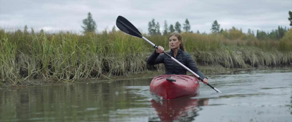 A woman is rowing her canoe near the tall grass