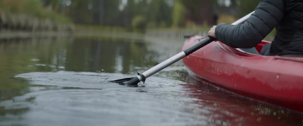 Woman paddles a red kayak down a river