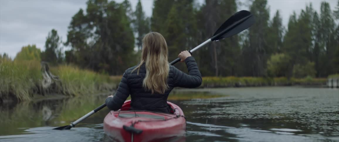 A woman is peddling a kayak down a calm river