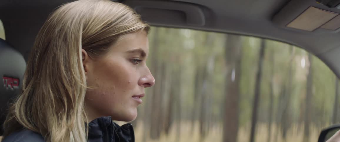 A woman drives a car down a rural forest road