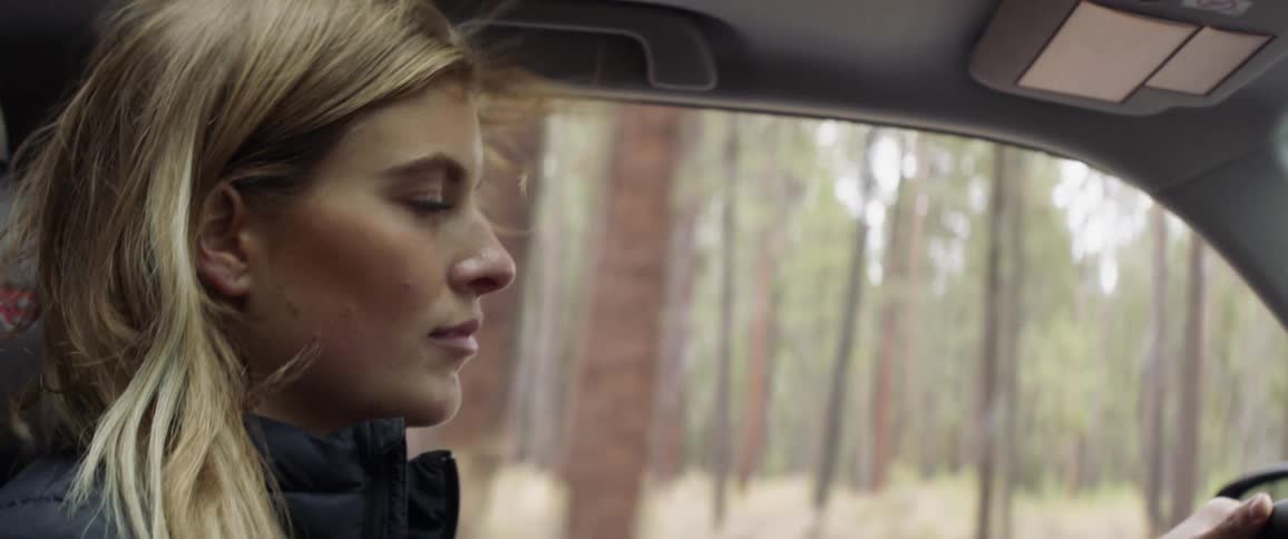 Woman driving a car on a country road surrounded by trees
