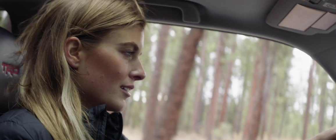 Woman driving a car on a country road surrounded by trees