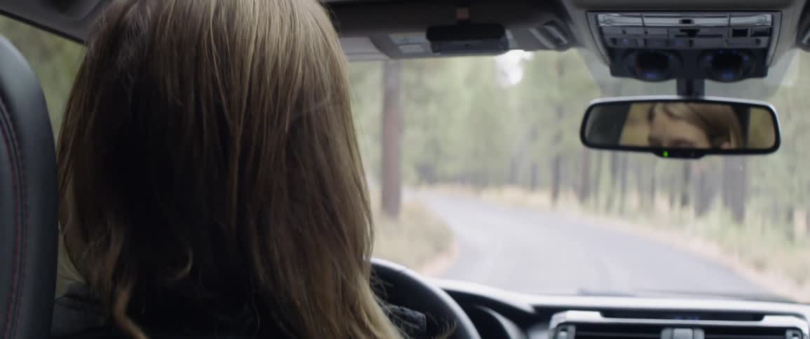 A woman steers a car on a road lined with trees