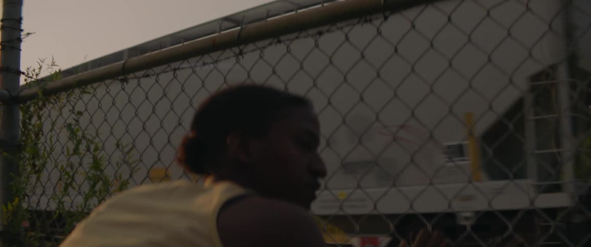 Woman watches a passing train through a chain link fence