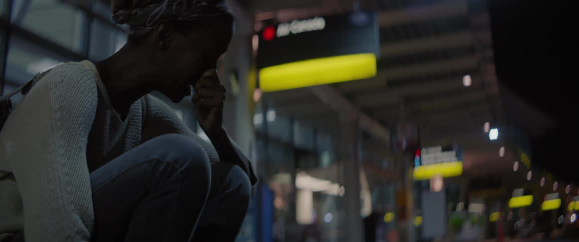 A woman is crying as she sits on a curb outside an airport at night