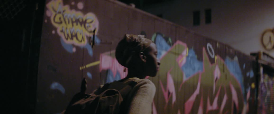 A person wearing a backpack walks past a wall covered in graffiti