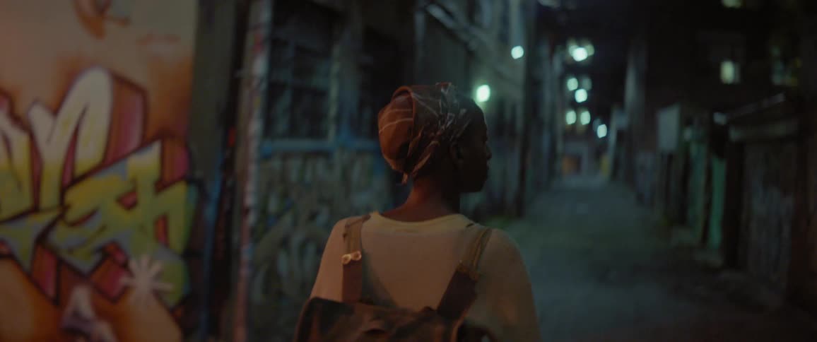A person wearing a backpack walks in an alley at night