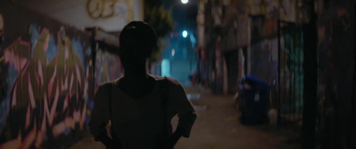 A woman is walking down an alley at night