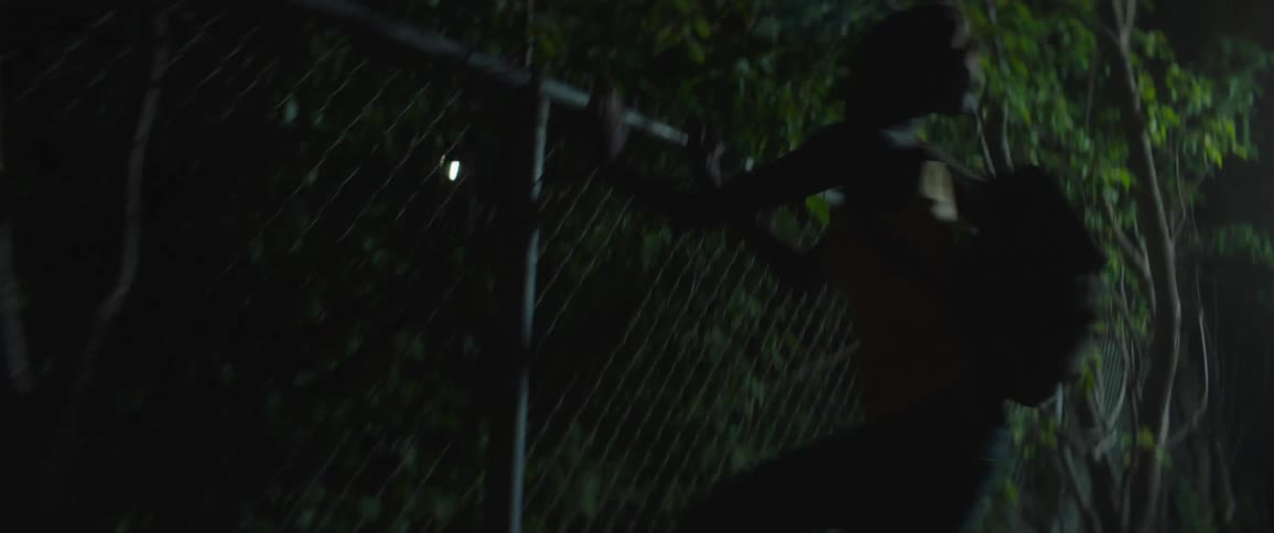 A girl jumps on a chain link fence at night
