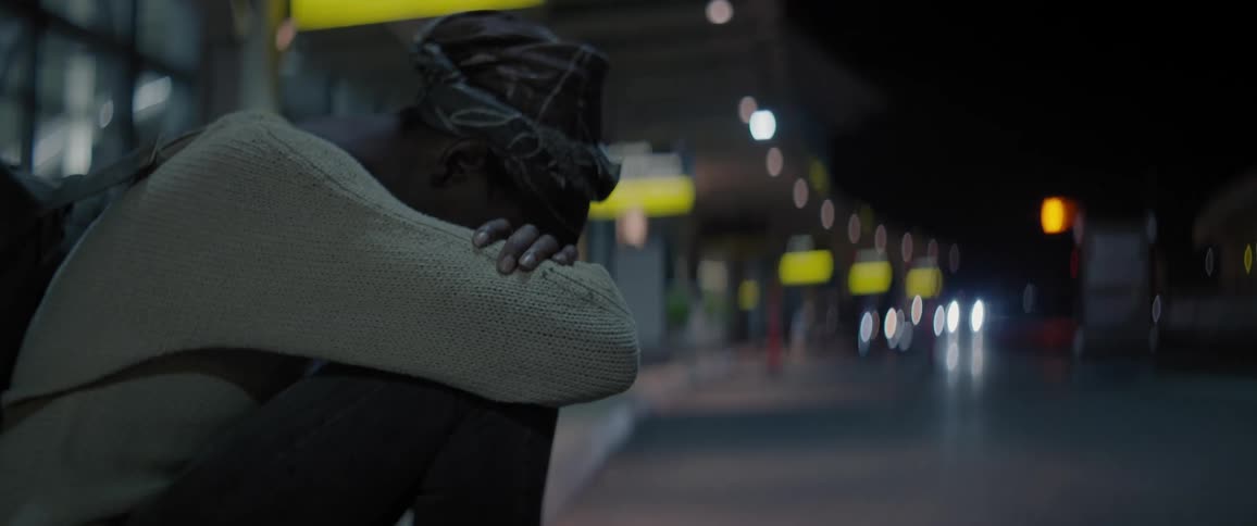 A woman sits on the sidewalk with her head in her arms