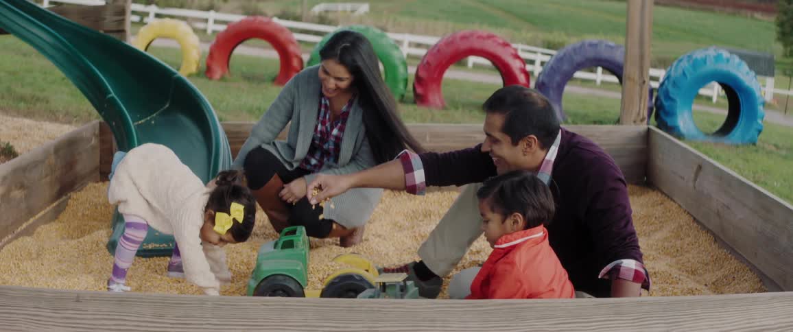 A family of four are playing in a sandbox on a playground