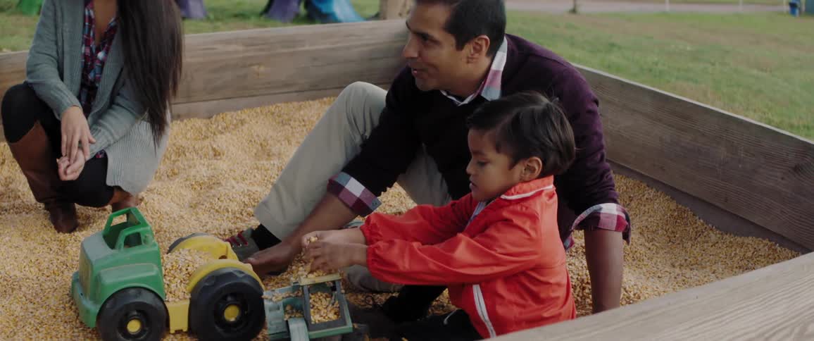 Parents and a child are playing with corn in a playpen