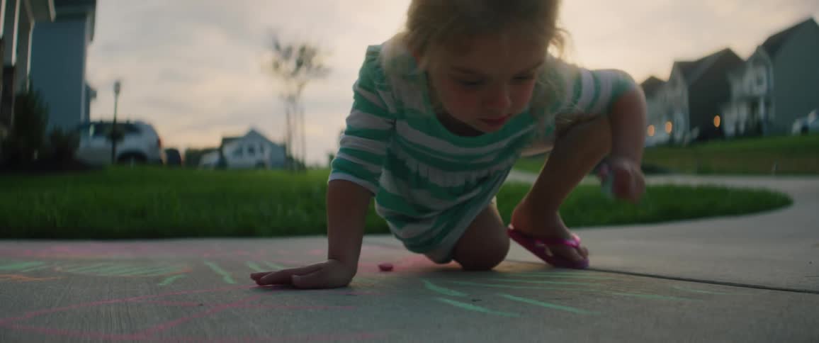 A girl is drawing with chalk on a sidewalk at dusk