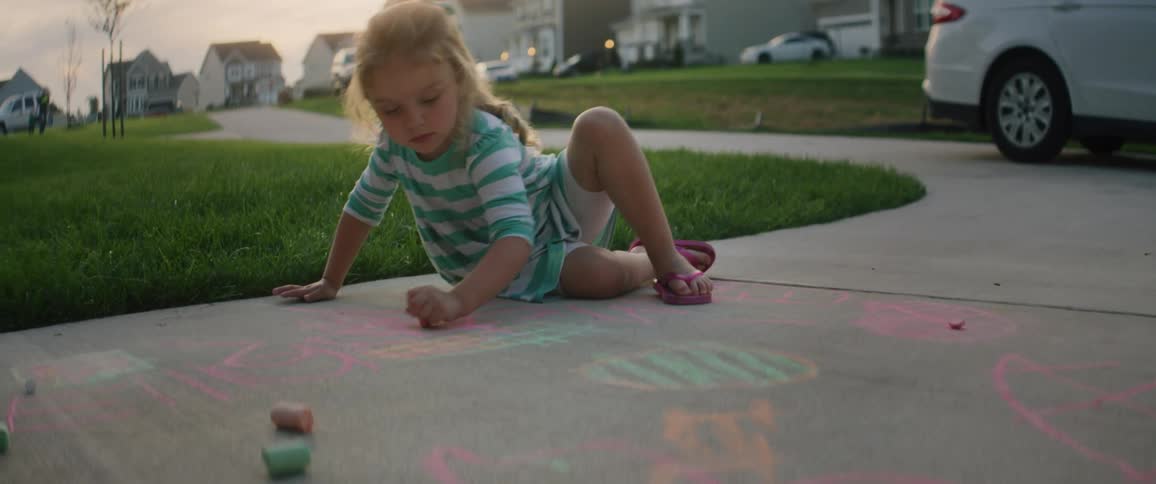 A young girl draws on a sidewalk with chalk