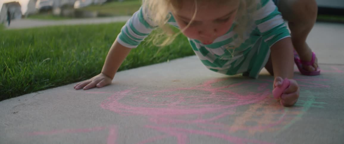 Young girl sits on sidewalk playing with sidewalk chalk