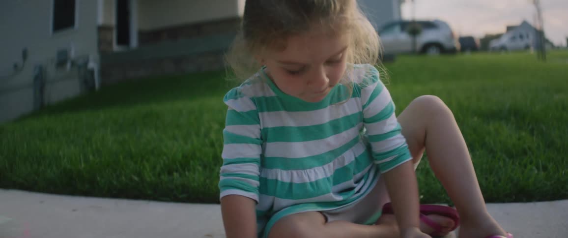 A young girl draws on a sidewalk with chalk